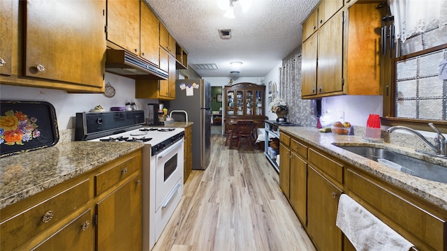 kitchen with sink, a textured ceiling, stainless steel appliances, light stone countertops, and light hardwood / wood-style floors