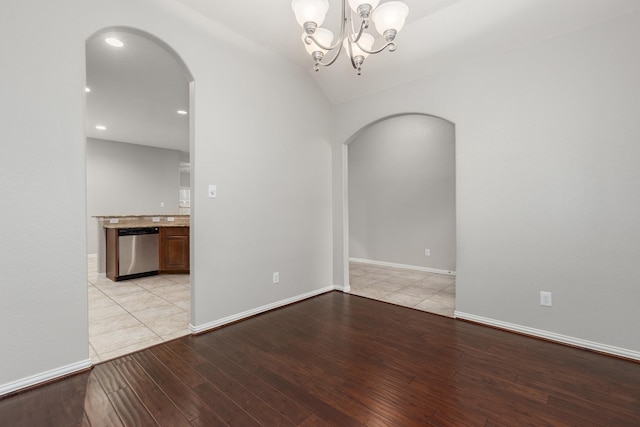 spare room featuring an inviting chandelier, vaulted ceiling, and light hardwood / wood-style floors