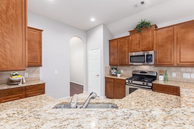 kitchen with light stone counters, sink, backsplash, and stainless steel appliances