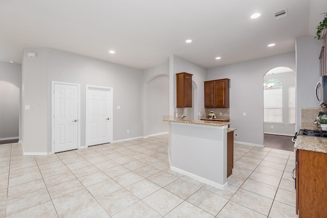 kitchen featuring light stone counters, tasteful backsplash, light tile patterned floors, appliances with stainless steel finishes, and kitchen peninsula