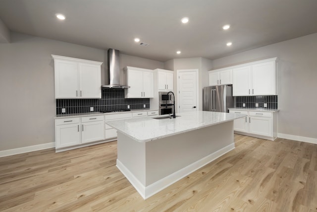 kitchen featuring white cabinetry, a center island with sink, stainless steel appliances, light hardwood / wood-style floors, and wall chimney range hood