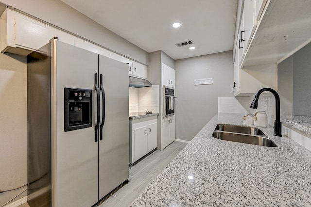 kitchen featuring sink, white cabinets, wall oven, stainless steel refrigerator with ice dispenser, and light stone countertops