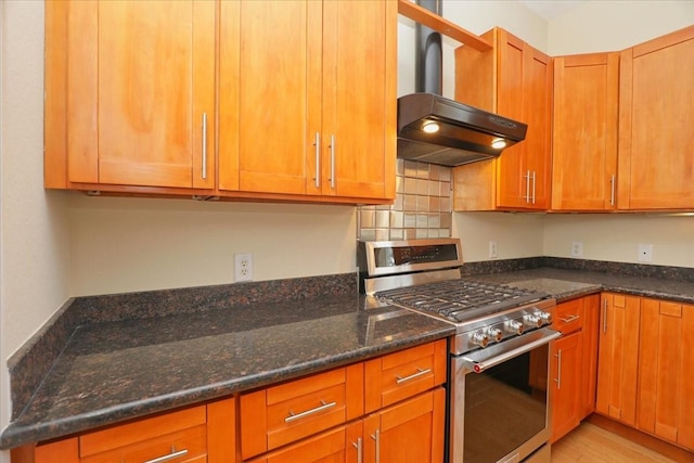 kitchen featuring range hood, stainless steel range with gas stovetop, and dark stone counters