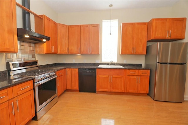 kitchen featuring sink, hanging light fixtures, stainless steel appliances, light hardwood / wood-style floors, and wall chimney range hood