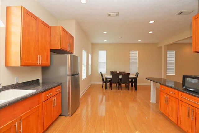 kitchen with sink, dark stone countertops, stainless steel fridge, and light wood-type flooring