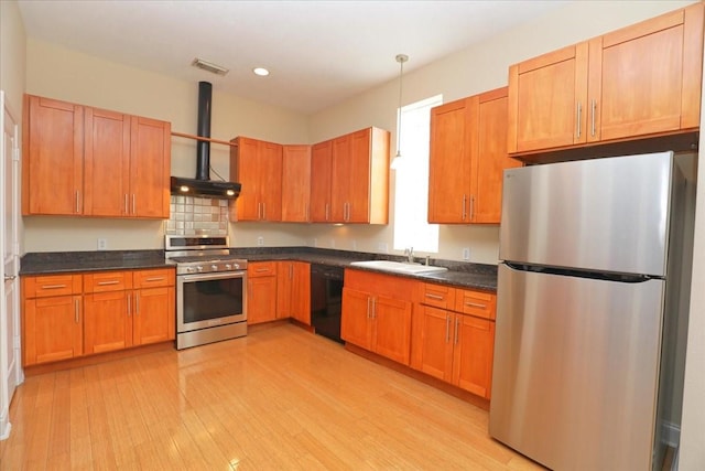 kitchen with appliances with stainless steel finishes, sink, hanging light fixtures, wall chimney range hood, and light wood-type flooring