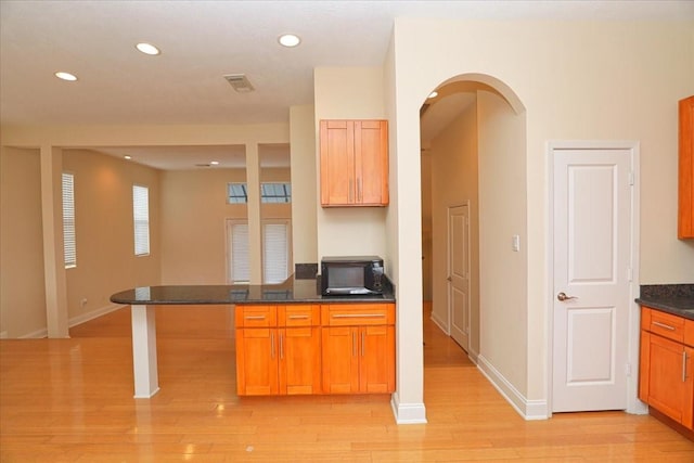 kitchen featuring a breakfast bar area, dark stone countertops, and light wood-type flooring