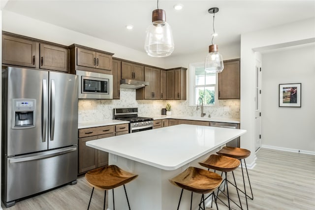 kitchen featuring a center island, stainless steel appliances, light countertops, under cabinet range hood, and pendant lighting