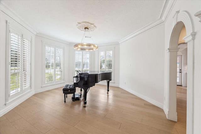 miscellaneous room with ornate columns, light hardwood / wood-style floors, crown molding, a textured ceiling, and an inviting chandelier