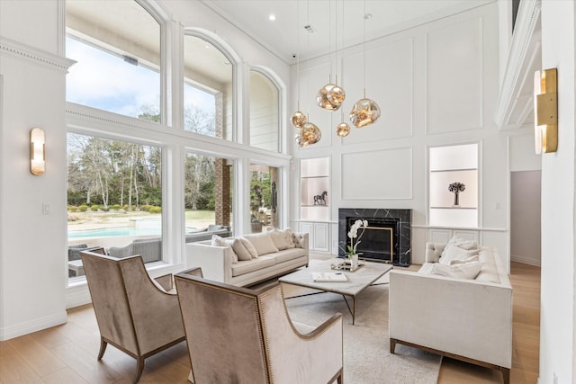 living room featuring light wood-type flooring, built in features, a premium fireplace, and a high ceiling