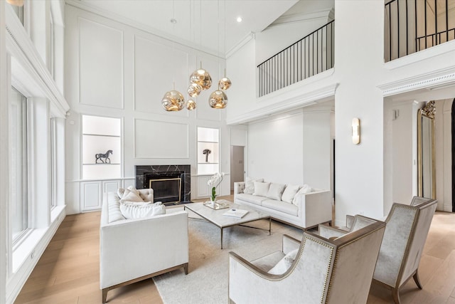 living room featuring a towering ceiling, built in features, a high end fireplace, and light hardwood / wood-style flooring