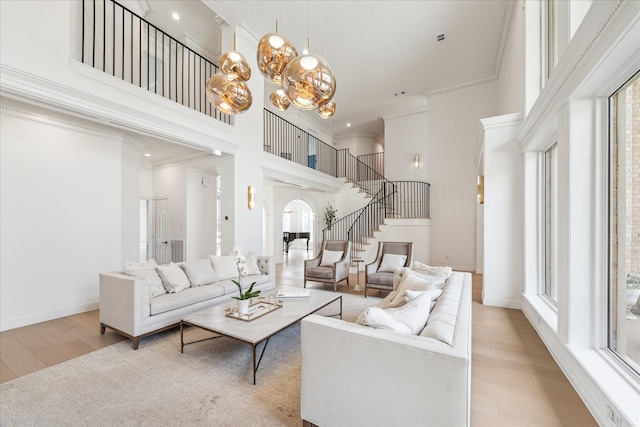 living room with ornamental molding, a towering ceiling, an inviting chandelier, and light hardwood / wood-style flooring