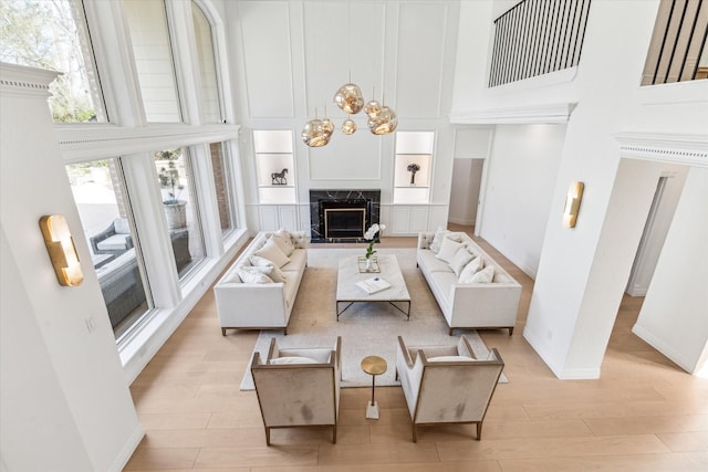 living room featuring a towering ceiling, a fireplace, a chandelier, and light wood-type flooring