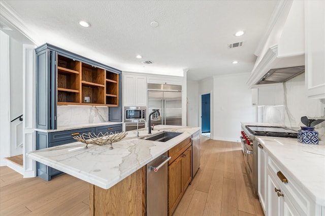 kitchen featuring a kitchen island with sink, built in appliances, light stone countertops, and white cabinets