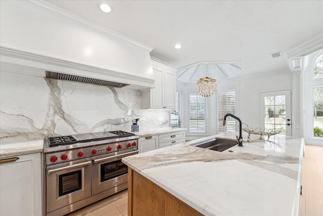 kitchen featuring white cabinetry, sink, range with two ovens, light stone counters, and a center island with sink