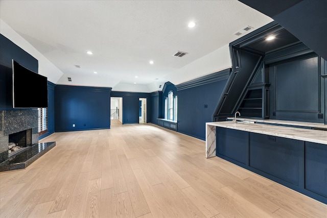 kitchen with light stone counters, a high end fireplace, sink, and light hardwood / wood-style floors