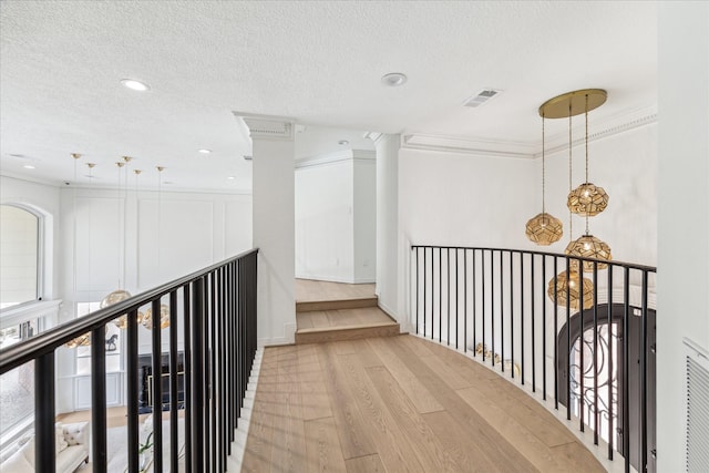 corridor featuring crown molding, light hardwood / wood-style flooring, decorative columns, and a textured ceiling