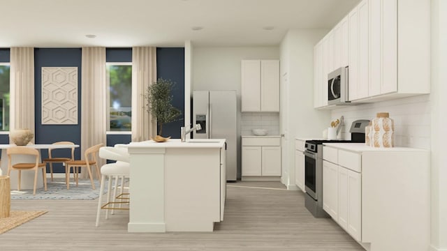 kitchen with light hardwood / wood-style flooring, a breakfast bar, appliances with stainless steel finishes, a kitchen island with sink, and white cabinets