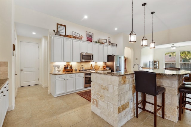 kitchen featuring appliances with stainless steel finishes, a kitchen breakfast bar, white cabinets, a center island with sink, and dark stone counters