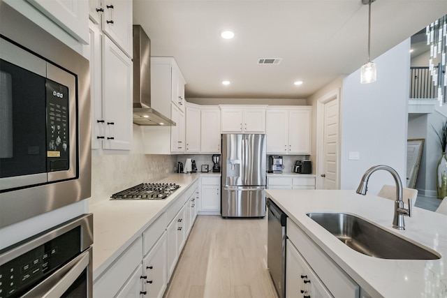 kitchen with sink, wall chimney range hood, pendant lighting, stainless steel appliances, and white cabinets