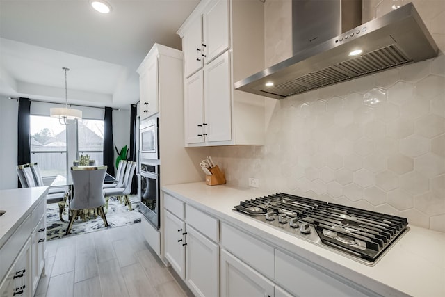 kitchen with white cabinetry, stainless steel appliances, hanging light fixtures, and exhaust hood