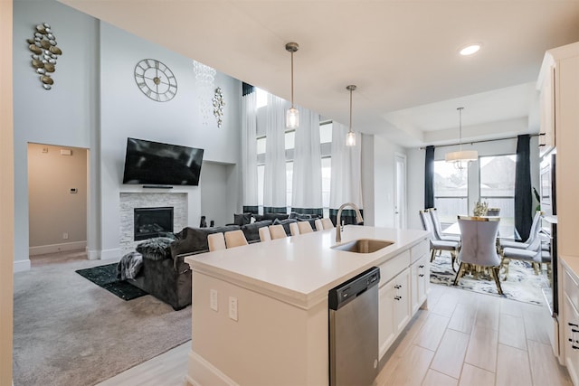 kitchen featuring an island with sink, dishwasher, sink, white cabinets, and hanging light fixtures