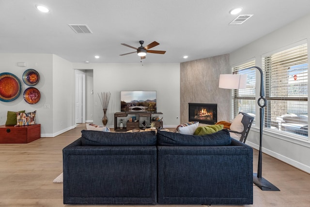 living room with light hardwood / wood-style flooring, a large fireplace, and ceiling fan