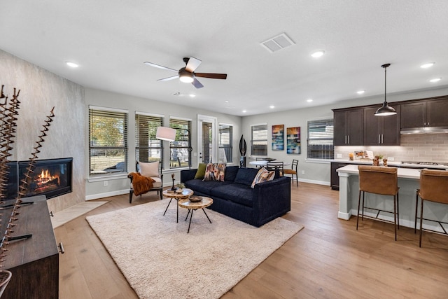 living room with a tile fireplace, ceiling fan, and light hardwood / wood-style flooring