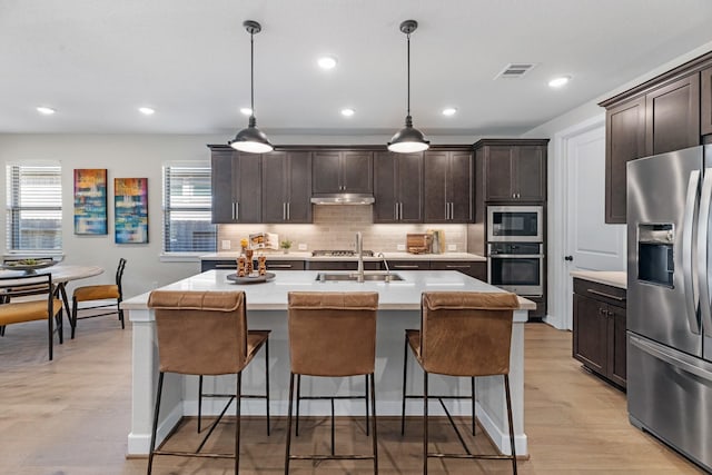 kitchen with a kitchen island with sink, hanging light fixtures, dark brown cabinetry, and appliances with stainless steel finishes