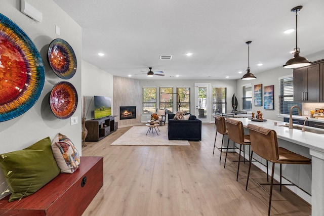 living room featuring a breakfast bar, pendant lighting, sink, dark brown cabinetry, and light wood-type flooring