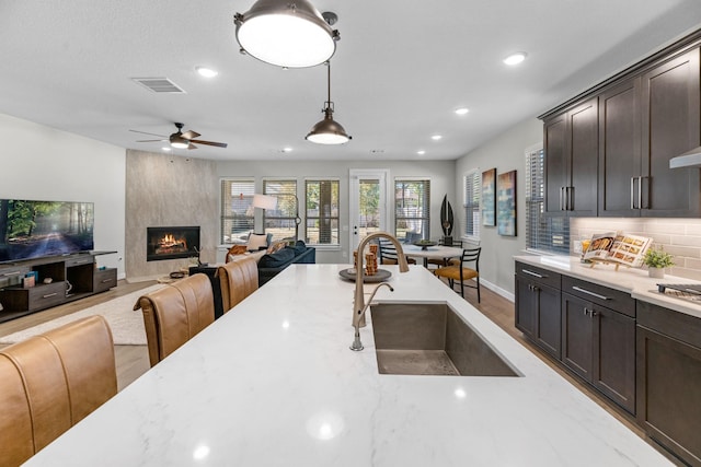 kitchen with light stone countertops, sink, dark brown cabinetry, and decorative light fixtures