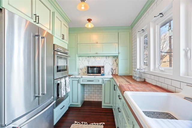 kitchen with sink, butcher block counters, stainless steel appliances, tasteful backsplash, and green cabinetry