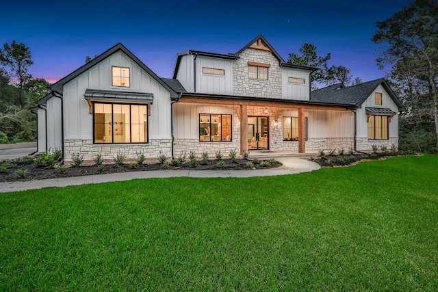 back of property with board and batten siding, stone siding, a yard, and a standing seam roof