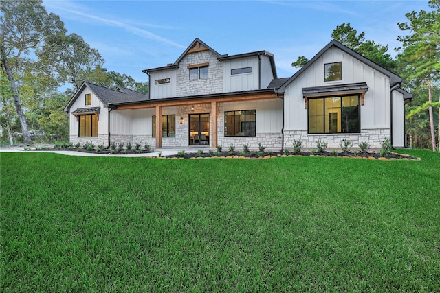 modern inspired farmhouse with stone siding, covered porch, board and batten siding, and a front yard