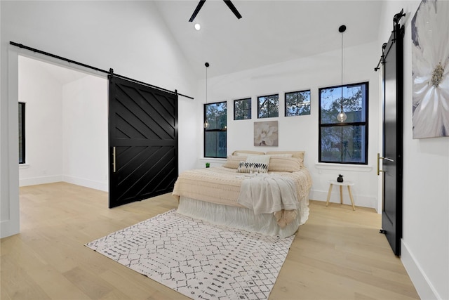 bedroom with high vaulted ceiling, a barn door, and light wood-type flooring