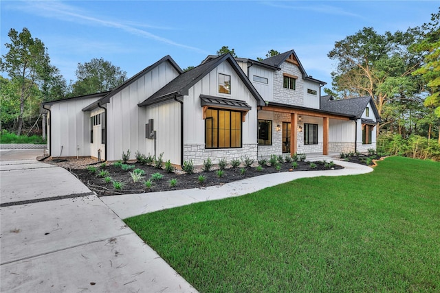 modern farmhouse with board and batten siding, a front yard, stone siding, and roof with shingles