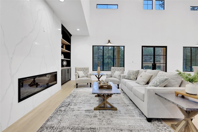 living room with built in shelves, recessed lighting, a premium fireplace, a towering ceiling, and light wood-style floors