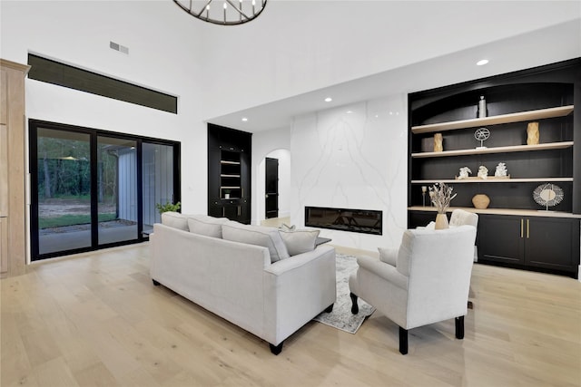 living area featuring arched walkways, a fireplace, visible vents, built in features, and light wood-style floors