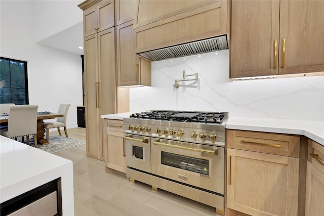 kitchen with light brown cabinets, ventilation hood, backsplash, double oven range, and light wood finished floors