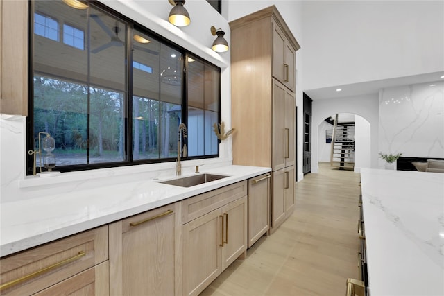 kitchen featuring light stone counters, arched walkways, a sink, and light brown cabinetry