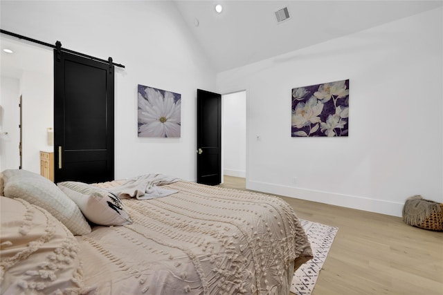 bedroom with visible vents, light wood-style flooring, a barn door, high vaulted ceiling, and baseboards