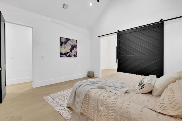 bedroom featuring light wood-style floors, visible vents, baseboards, and a barn door