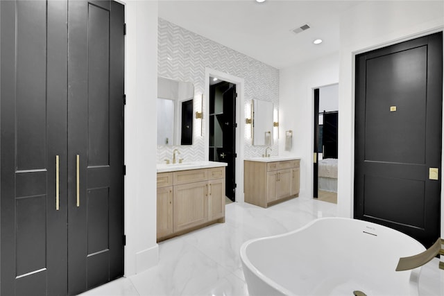 bathroom featuring visible vents, a soaking tub, a sink, marble finish floor, and two vanities