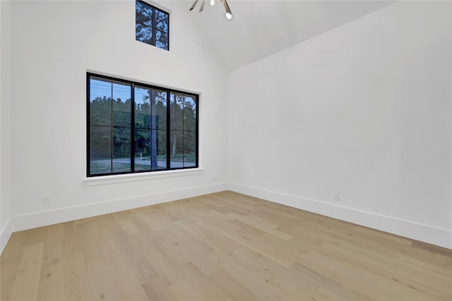 empty room featuring high vaulted ceiling, wood finished floors, and baseboards