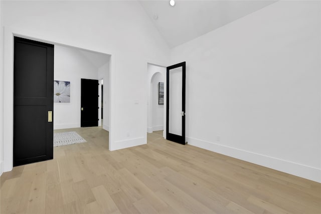 unfurnished room with high vaulted ceiling, arched walkways, baseboards, and light wood finished floors