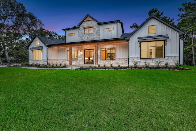 modern farmhouse style home featuring a standing seam roof, stone siding, a front lawn, and board and batten siding