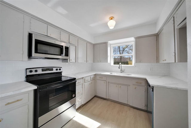 kitchen with sink, light hardwood / wood-style flooring, gray cabinets, backsplash, and stainless steel appliances