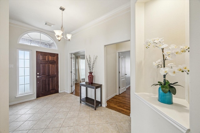 tiled foyer with ornamental molding, plenty of natural light, and a chandelier