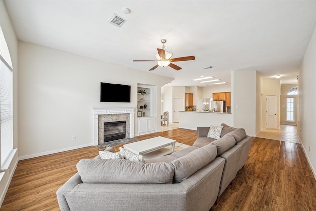 living room featuring light hardwood / wood-style flooring, built in features, and ceiling fan