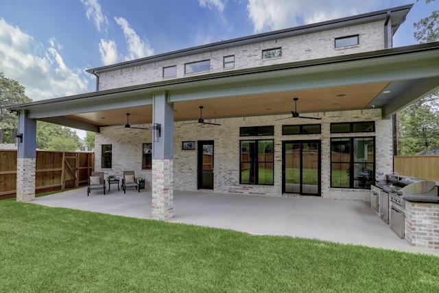 rear view of property with ceiling fan, area for grilling, a patio, and a lawn